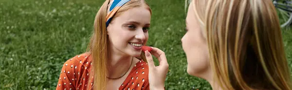A young woman feeds her girlfriend a berry during a summer picnic in a park. — Stock Photo