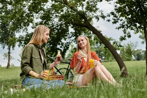 Due giovani donne si godono un pranzo al sacco in un parco, condividendo panini e risate. — Foto stock