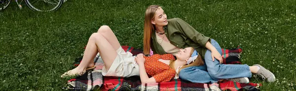 Dos mujeres jóvenes comparten un momento romántico mientras yacen sobre una manta en un parque verde. - foto de stock