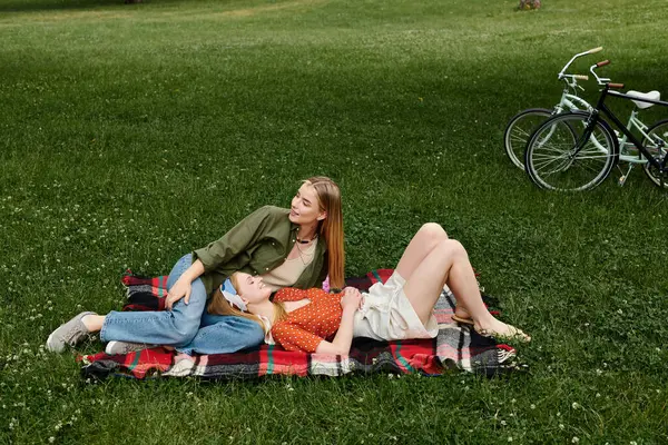 Zwei junge Frauen entspannen sich auf einer Decke in einem Park, eine legt den Kopf in den Schoß der anderen und genießt einen sonnigen Nachmittag. — Stockfoto