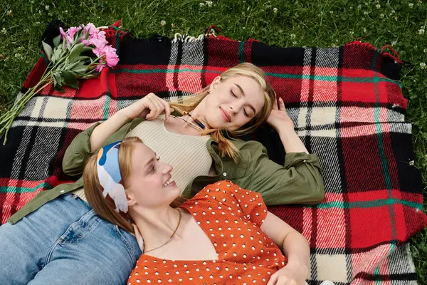 Two young women relax on a checkered blanket in a grassy park, enjoying each others company. — Stock Photo