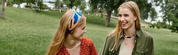 Two young women walk side-by-side in a green park, smiling and enjoying each other company. — Stock Photo