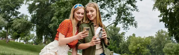 Ein lesbisches Paar genießt einen sonnigen Nachmittag im Park und schaut auf sein Handy. — Stockfoto