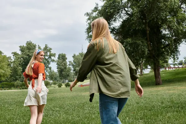 Two young women playfully chase each other in a green park on a sunny day. — Stock Photo