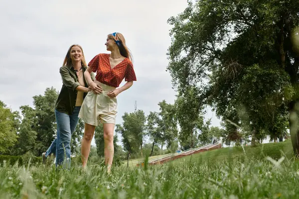 Duas jovens mulheres riem e se abraçam, desfrutando de uma tarde ensolarada em um parque verde. — Fotografia de Stock