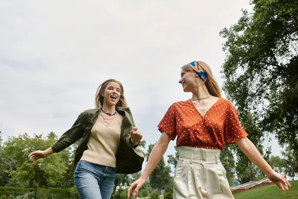 Deux jeunes femmes rient et courent dans un parc verdoyant, profitant d'une journée d'été insouciante. — Photo de stock