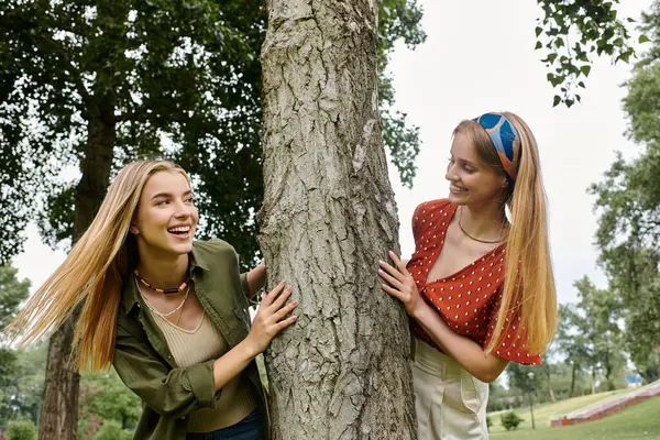 Two young women share a playful moment, leaning against a tree and laughing. — Stock Photo
