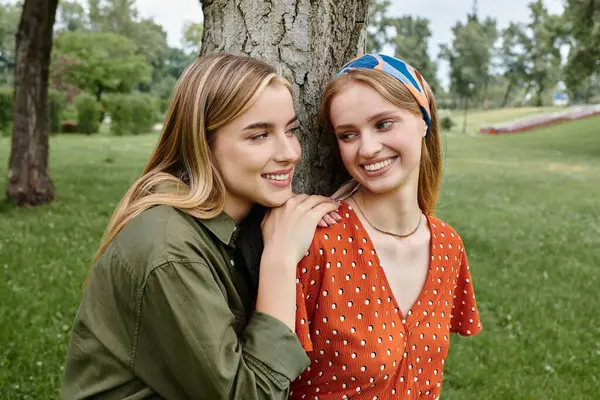 A lesbian couple enjoys a sunny afternoon in the park, leaning against a tree and sharing a smile. — Stock Photo