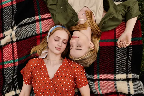 Two women lie on a checkered blanket in a green park, their eyes closed in peaceful slumber. — Stock Photo