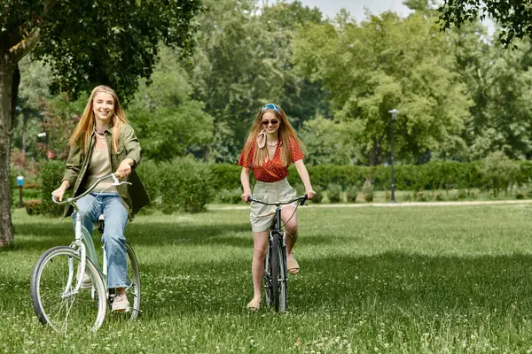 Two young women, a lesbian couple, enjoy a bike ride together in a green park. — Stock Photo