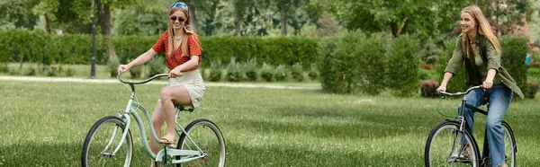 Duas jovens mulheres andam de bicicleta em um parque verde em um dia ensolarado. — Fotografia de Stock