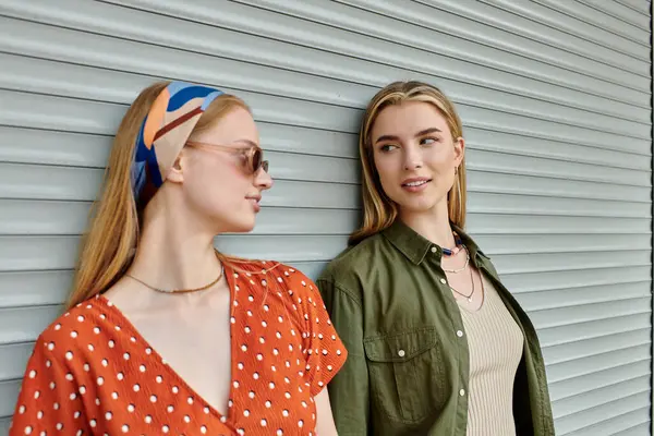 Two young women, one in a red polka dot dress and the other in a green shirt, stand close together and smile as they look at each other. — Stock Photo