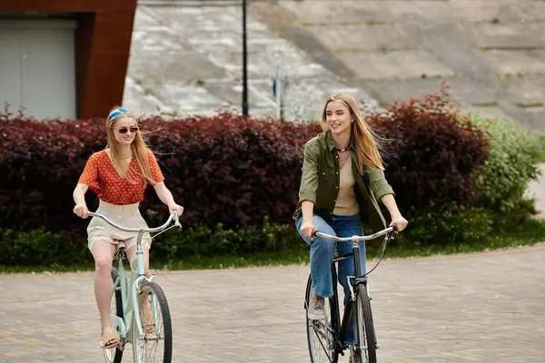 Two young women enjoy a sunny afternoon bike ride in the park, their smiles reflecting the joy of their love. — Stock Photo