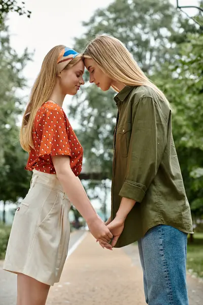 A lesbian couple holds hands and leans in close to each other in a lush green park. — Stock Photo