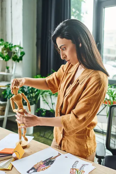 Una mujer de Oriente Medio trabaja en un proyecto de diseño de moda en su oficina, colocando cuidadosamente un maniquí de madera para inspirar su trabajo. - foto de stock