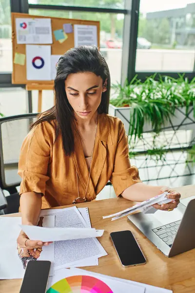 A woman with dark brown hair sits at her desk, reviewing papers and documents. — Stock Photo