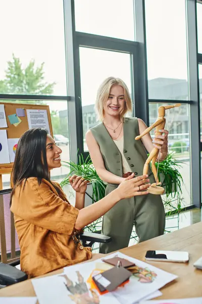 Two women discuss designs using a wooden mannequin in a modern office setting. — Stock Photo