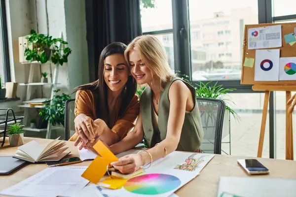 Two women, lesbian couple, collaborate on a project in a modern agency workspace, discussing color palettes and designs. — Stock Photo