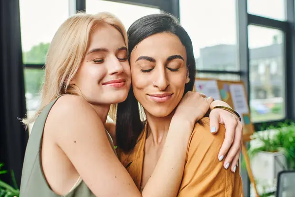 Two women embrace in a cozy workspace, showcasing their connection and professional success. — Stock Photo