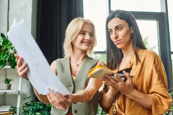 Two young women in a modern office setting work together on a project, reviewing documents and discussing ideas. — Stock Photo