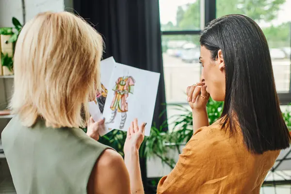 Deux jeunes femmes dans un espace de travail moderne passent en revue un croquis de design de mode. — Photo de stock