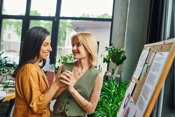 Lesbisches Paar in einem modernen Büro, Händchen haltend und lächelnd, eine kollaborative und unterstützende Arbeitsumgebung zeigend. — Stockfoto