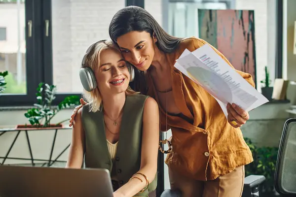 Duas mulheres trabalham em um projeto em um escritório moderno, rindo e compartilhando um momento de conexão. — Fotografia de Stock