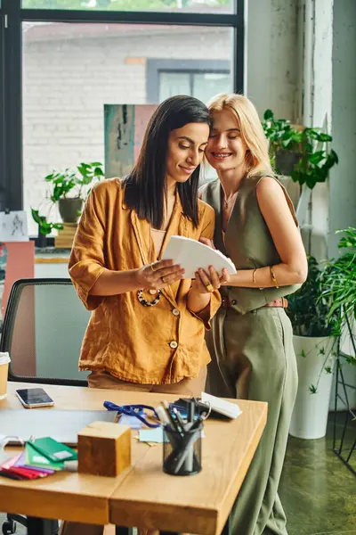 Two young women, wearing smart casual attire, work together on a project in a cozy workspace. — Stock Photo
