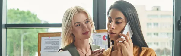 Two women in professional attire work on a project in a modern agency. One talks on phone while other looks focused, lesbian couple — Stock Photo