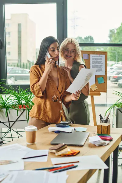 Lesbian couple in a modern workspace collaborate on a project, one on the phone and the other reviewing a document. — Stock Photo