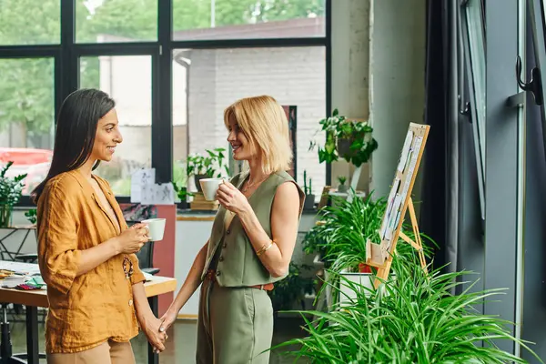 Two women in a modern office space share a coffee break and a smile during a work project. — Stock Photo