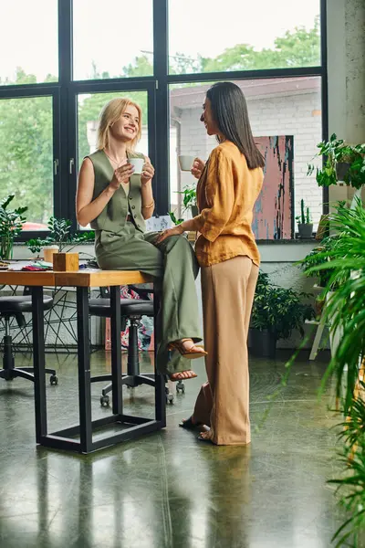 Two women in a modern office setting share coffee and a conversation. — Stock Photo