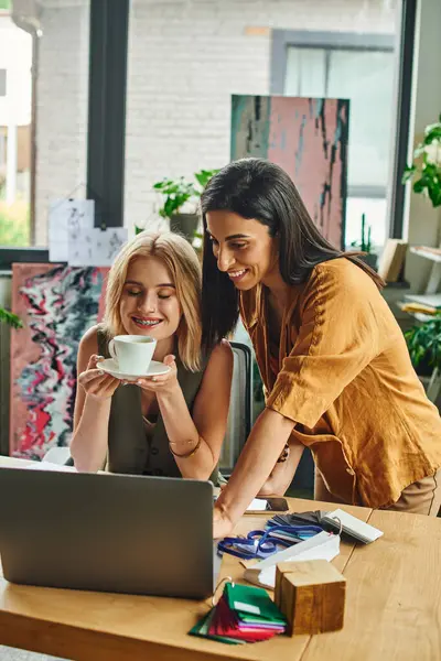 Two women in smart casual attire collaborate on a project at a cozy, modern agency. They chat over coffee with design samples on the table — Stock Photo
