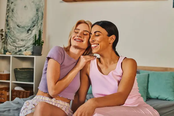 A happy lesbian couple, an interracial pair, share a warm hug in their cozy living room. — Stock Photo