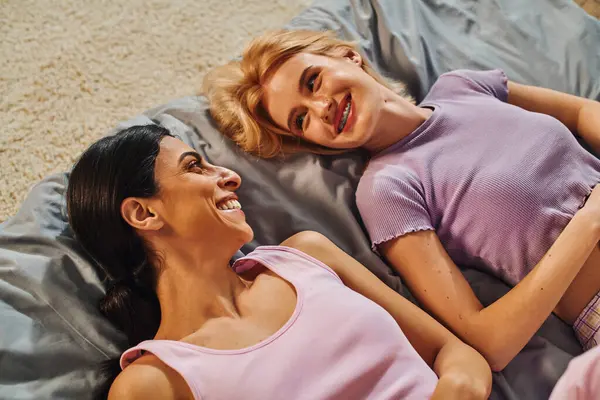 Um casal lésbico feliz deita-se na cama, rindo e gostando da companhia um do outro. — Fotografia de Stock