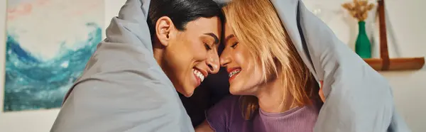A happy lesbian couple cuddles under a blanket in their home, sharing a sweet moment. — Stock Photo