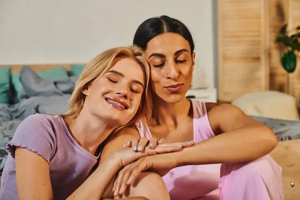 A happy lesbian couple cuddles close on a bed, their eyes closed in peaceful contentment. — Stock Photo