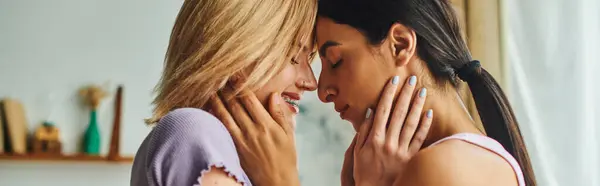 Due donne, una con i capelli biondi e l'altra con i capelli scuri, si abbracciano e si sorridono in un accogliente ambiente domestico. — Foto stock