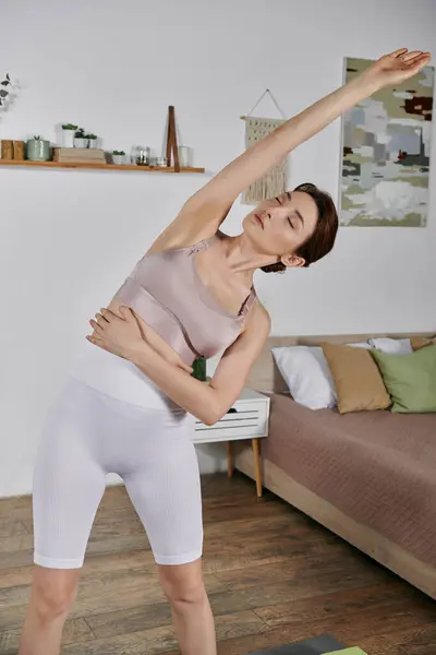 Una donna in un crop top esegue un tratto di yoga, raggiungendo il braccio verso il soffitto in un luminoso appartamento moderno. — Foto stock