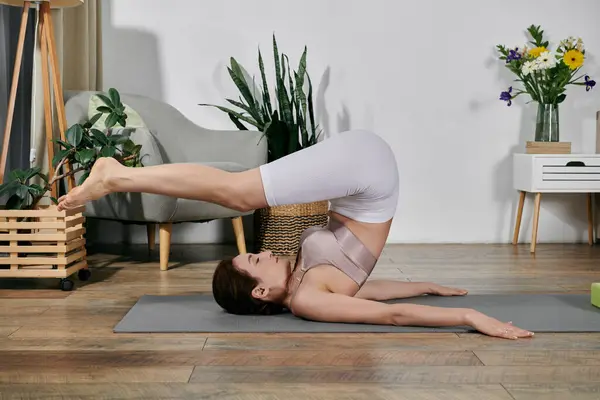 An Asian woman practices yoga in her apartment, performing a headstand with legs extended towards the ceiling. — Stock Photo