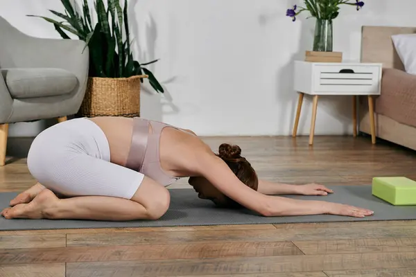 A beautiful Asian woman in a crop top practices yoga and meditation at home, on a gray mat. — Stock Photo