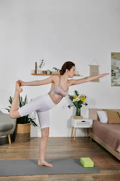 A beautiful Asian woman practices yoga in a modern apartment, balancing on one leg while reaching her other arm out. — Stock Photo