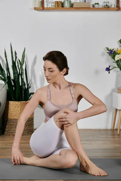 A beautiful Asian woman in a crop top sits on a yoga mat, practicing a seated pose in a modern apartment. — Stock Photo