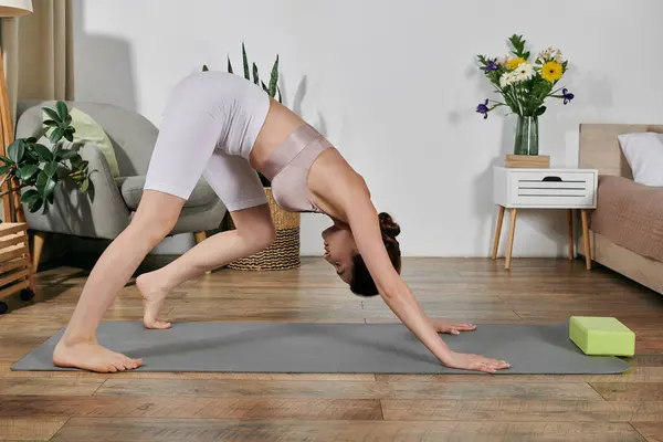 A beautiful Asian woman in a crop top and white shorts performs a yoga pose on a mat in her modern apartment. — Stock Photo