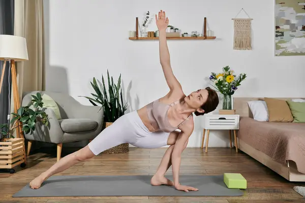 A woman in a crop top performs a yoga pose on a mat, stretching and reaching towards the ceiling. — Stock Photo