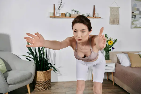 A beautiful Asian woman in a crop top practices yoga and meditation at home, in a modern apartment. — Stock Photo