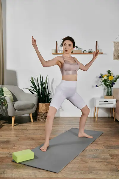 A young woman in a crop top performs a yoga pose on a mat in a modern apartment. — Stock Photo