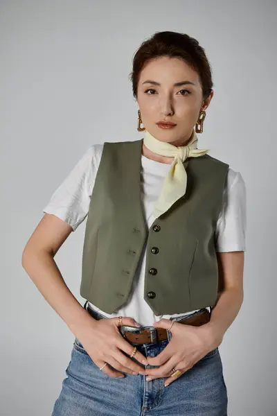 A fashionable Asian woman in a green vest and white t-shirt poses with a confident expression, her hands resting on her waist. — Stock Photo
