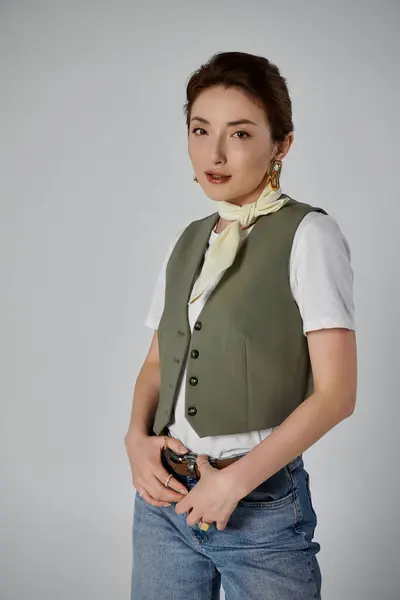 Uma mulher asiática elegante em um colete verde e camisa branca posa contra um pano de fundo cinza. — Fotografia de Stock