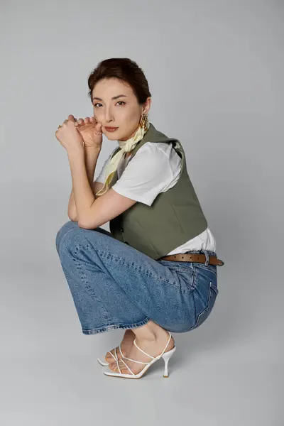 A beautiful Asian woman poses in a green vest and a neck scarf against a grey background. — Stock Photo